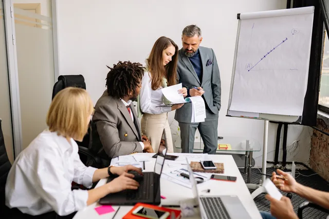 Business professionals collaborating in a modern office meeting with charts and laptops. Defining a sales development team's remit