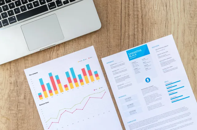 Top view of a laptop, charts, and resume on a wooden desk, showcasing business analysis and job application. Monitoring workload without rewarding meaningless activity