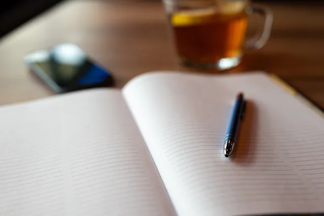 An open notebook with a pen, smartphone, and tea on a wooden table. Perfect for planning and relaxing settings. Opening with a relevant reason rather than fake familiarity