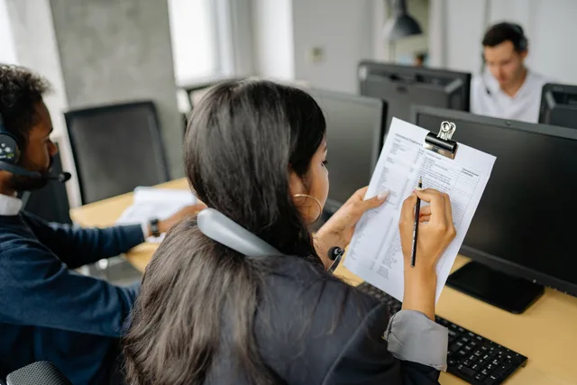Focused call center employee reviewing documents while on a call in an office setting. Sales call preparation